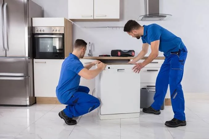 Two appliance technicians positioning a dishwasher in a residential kitchen
