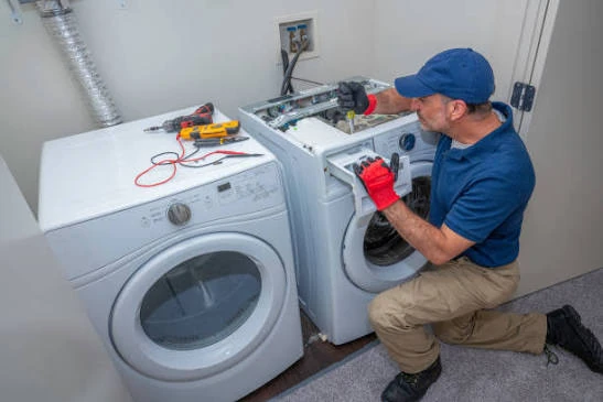 Technician repairing a washing machine beside a matching dryer
